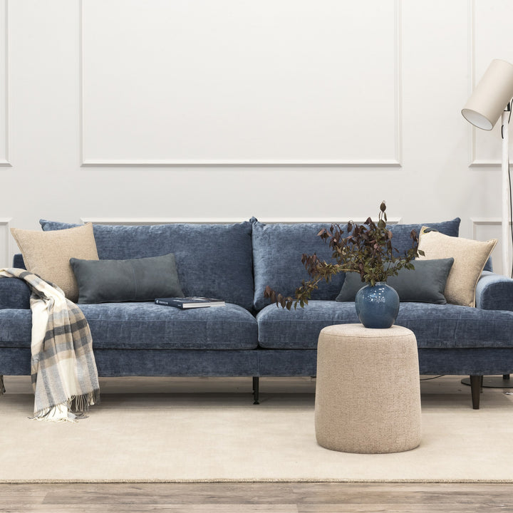 Leon sofa i denimblå chenille i lyst rom med panelvegg, beige puff og rutete pledd