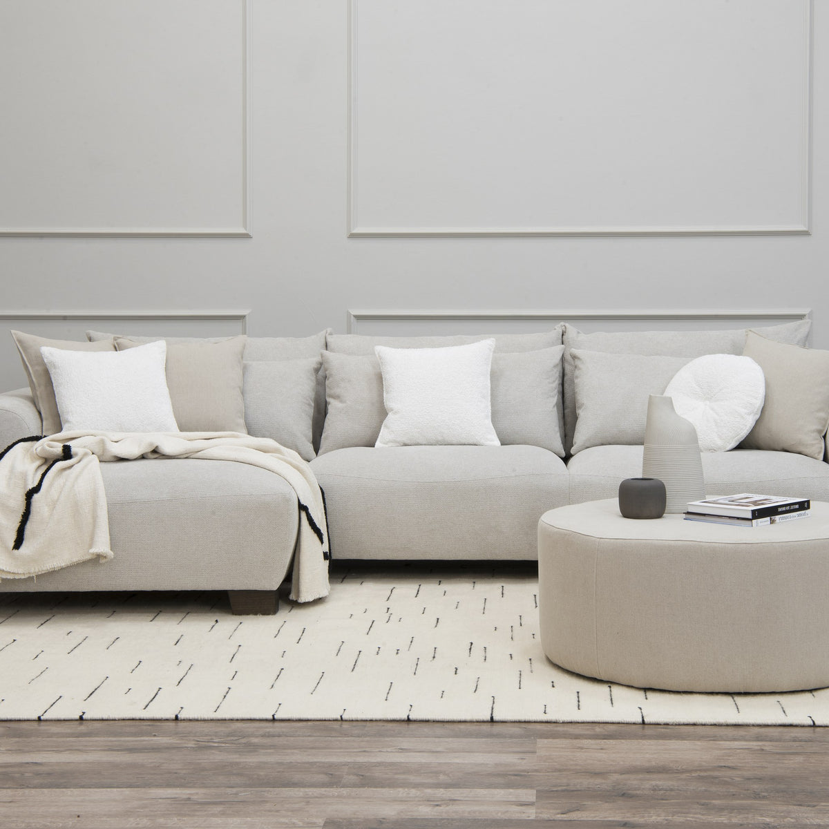 Smooth hjørnesofa i lys grå med venstrevendt sjeselong, lyst rom med rund puff og mønstret teppe