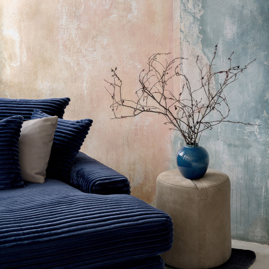 Tuva Xdeep daybed i mørk blå kordfløyel, hjørne med puter, ved sidebord med blå vase og grener.
