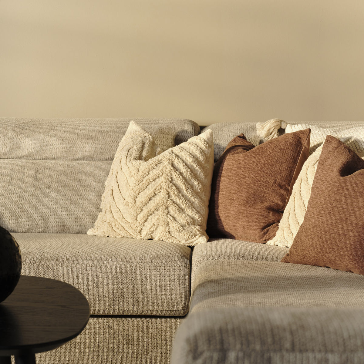 Fiskebein putetrekk i krem med vevd sildebensmønster på en beige sofa med brune puter