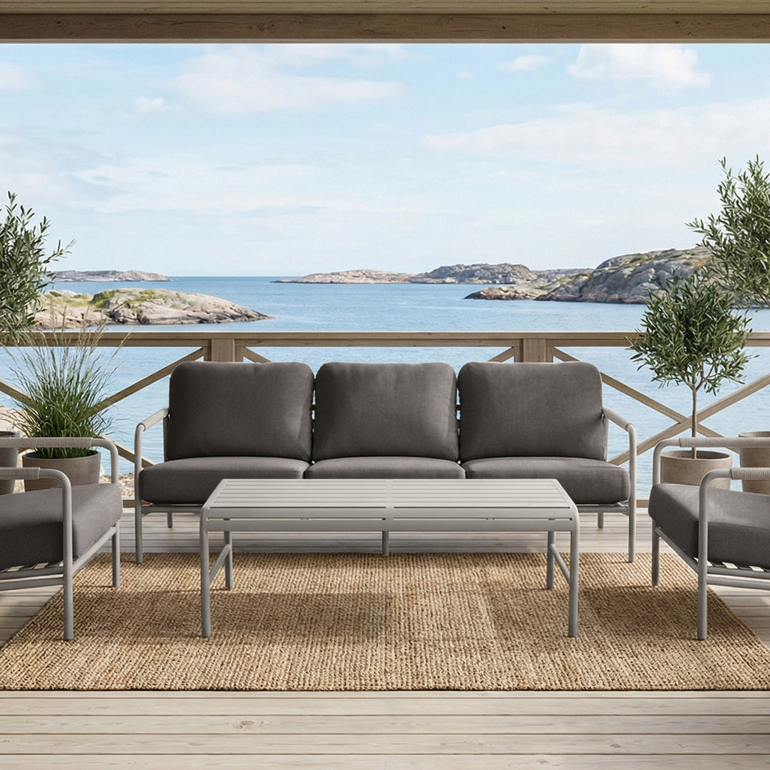Cantos sofagruppe med mørk grå puter og hvit ramme på terrasse med havutsikt og oliventrær
