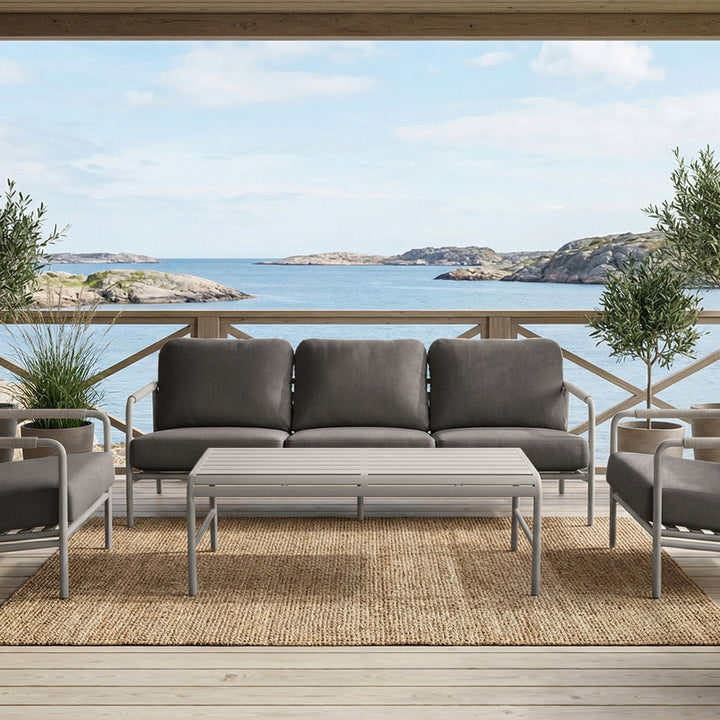 Cantos sofagruppe med mørk grå puter og hvit ramme på terrasse med havutsikt og oliventrær