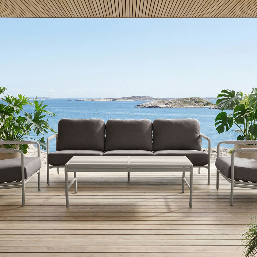 Cantos sofagruppe med mørk grå puter og lyst understell på en terrasse med utsikt over sjøen