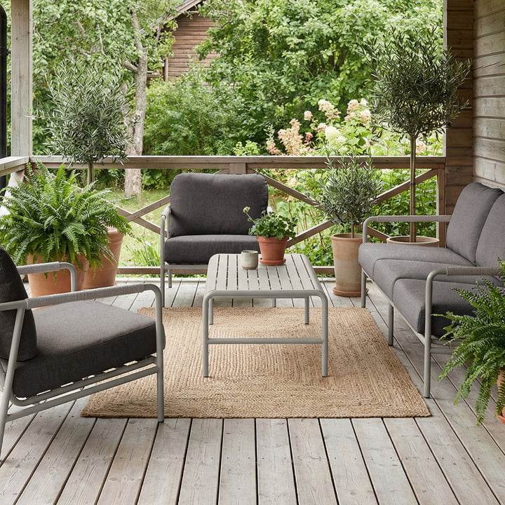 Cantos sofagruppe med mørk grå puter og lys ramme på terrasse med juteteppe, planter og hytte