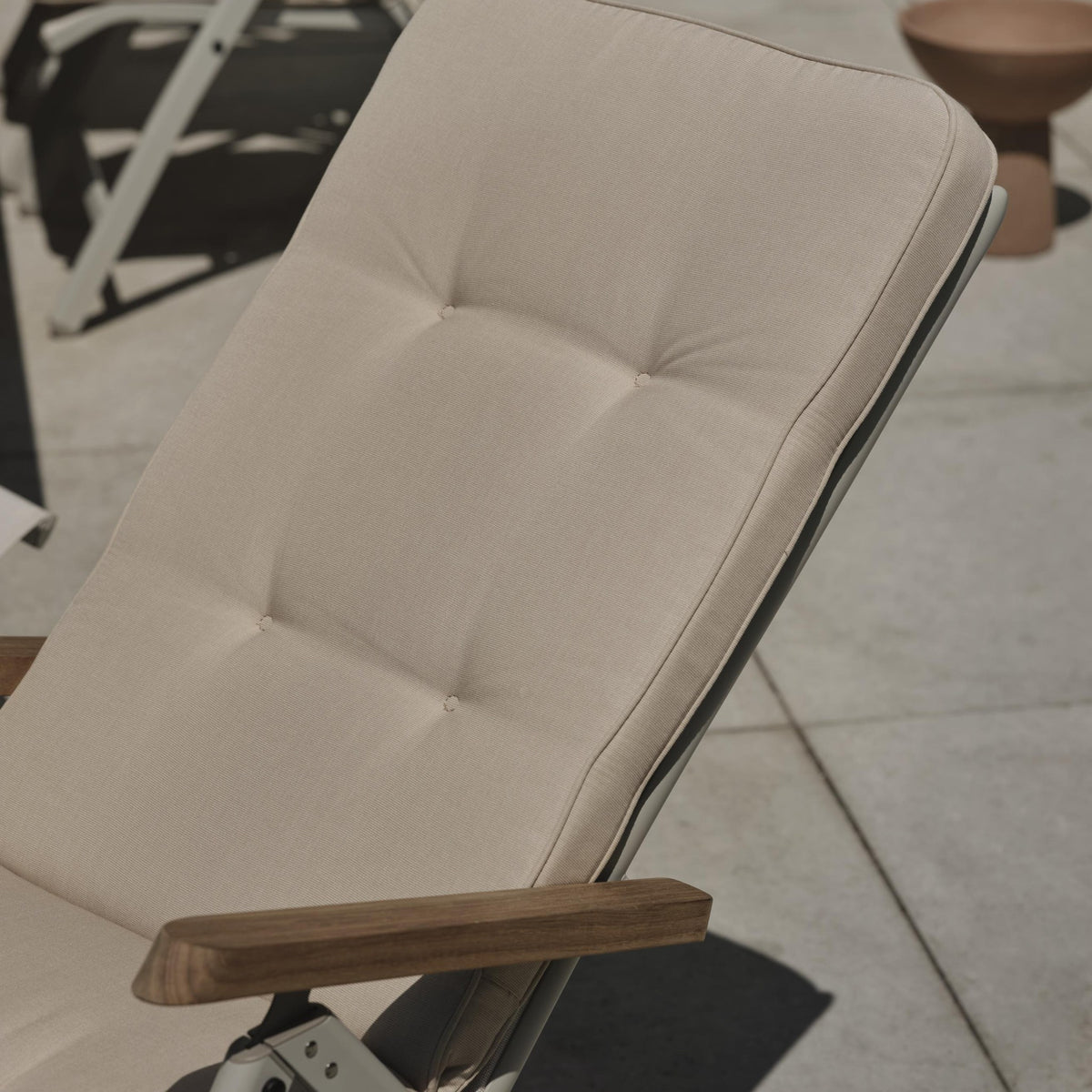 Brafab Iduna hagepute i beige, på sammenleggbar stol med teakarmlener på en steinterrasse ute
