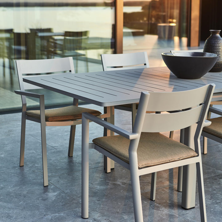 Brafab Frisk sittepute i gråbrun på hvite aluminiumsstoler ved spisebord på terrasse med glassvegg