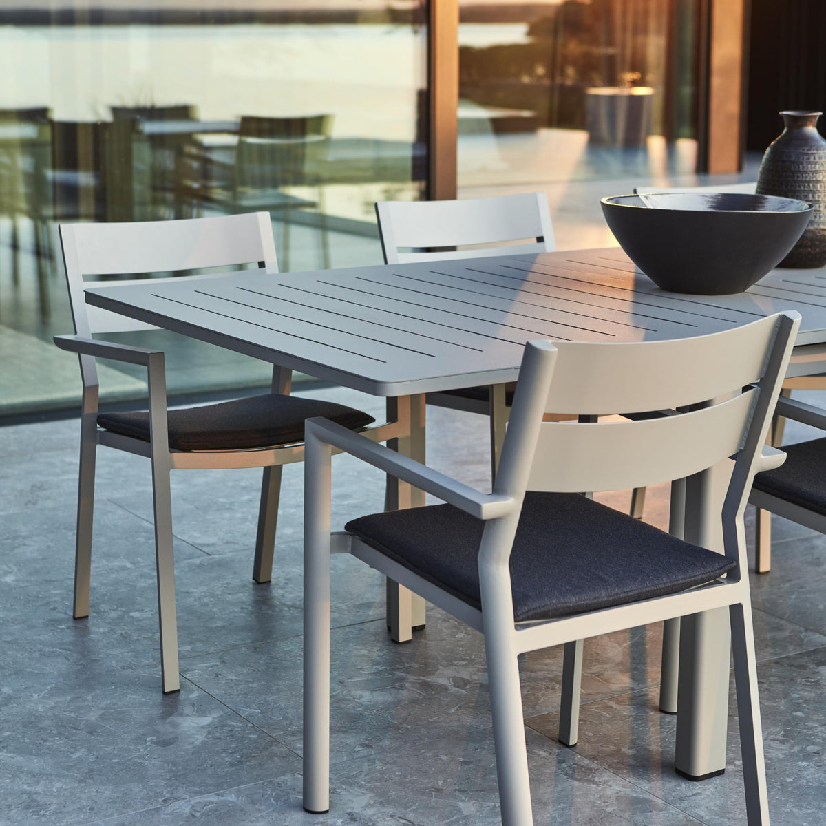 Brafab Frisk sittepute i sort på hvite aluminiumsstoler ved spisebord på terrasse med glassvegg