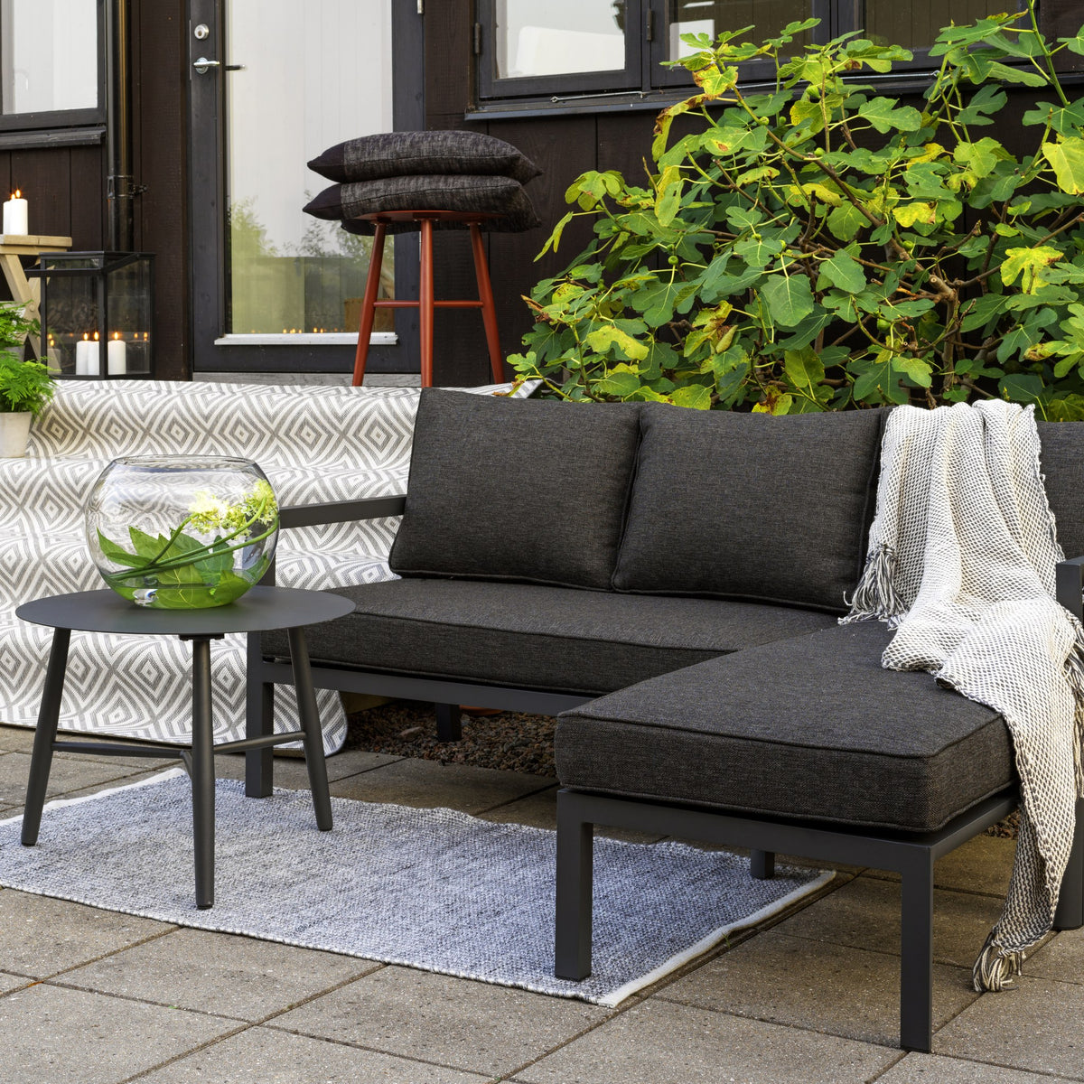 Brafab Delia utesofa i antrasitt med sjeselong på terrasse ved sort hus, grønn busk og pledd