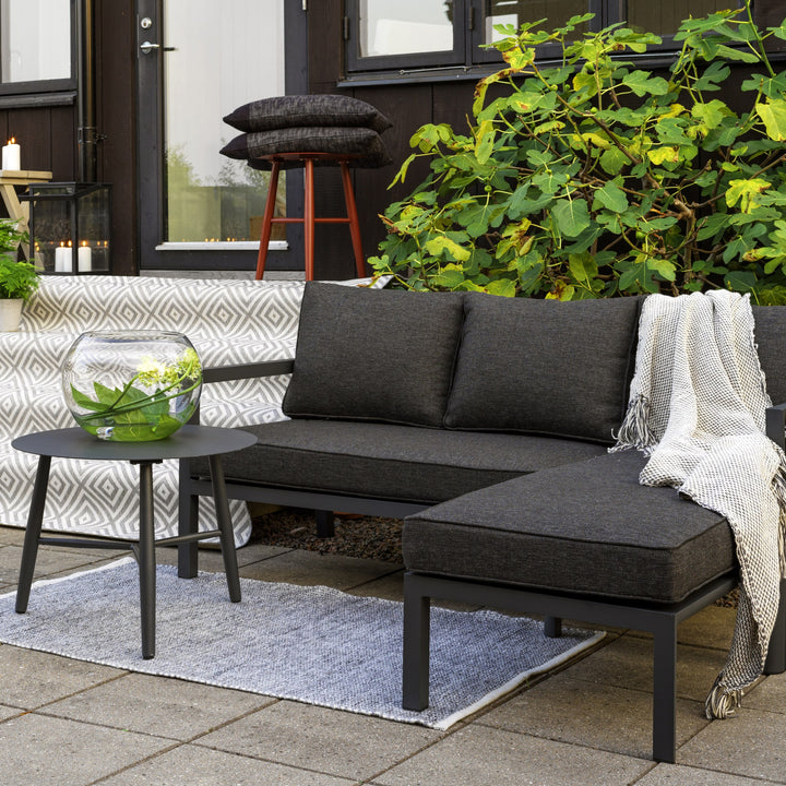 Brafab Delia utesofa i antrasitt med sjeselong på terrasse ved sort hus, grønn busk og pledd