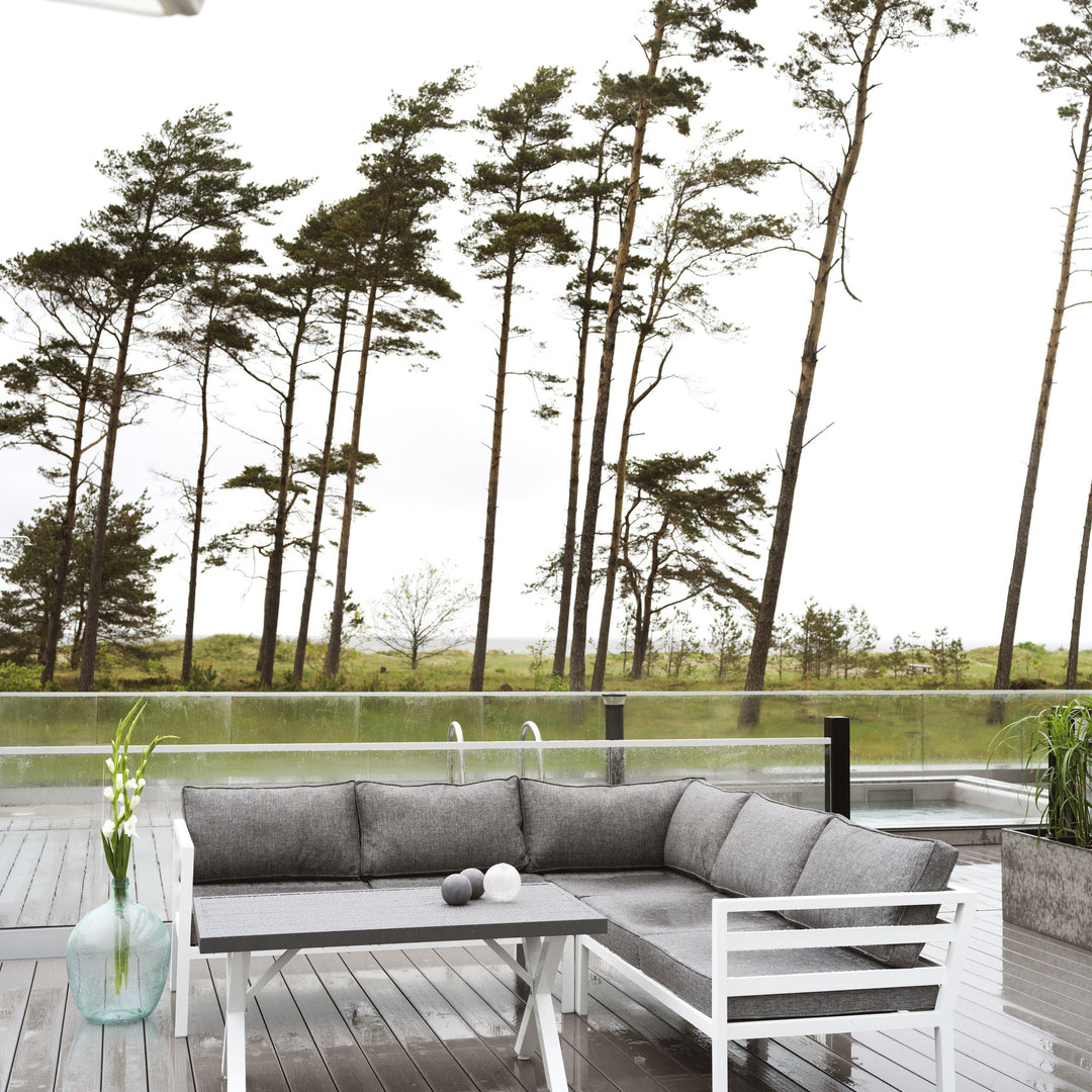 Brafab Weldon utesofa med grå puter og hvit ramme på terrasse med furutrær og kveldslys