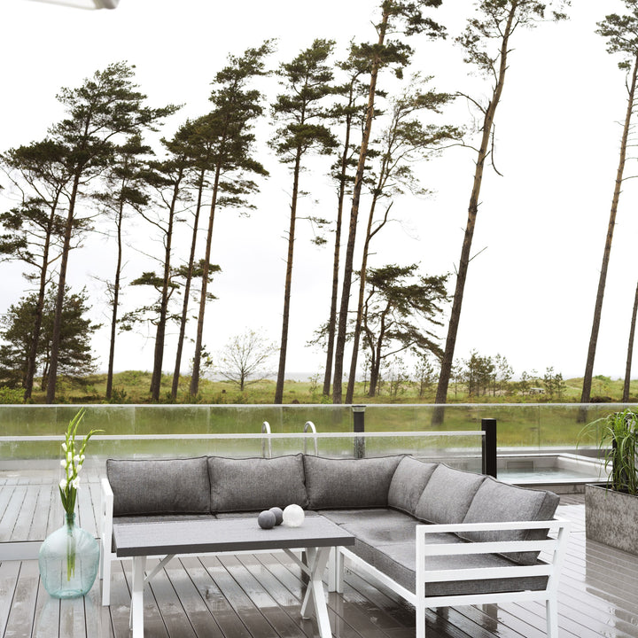 Brafab Weldon utesofa med grå puter og hvit ramme på terrasse med furutrær og kveldslys