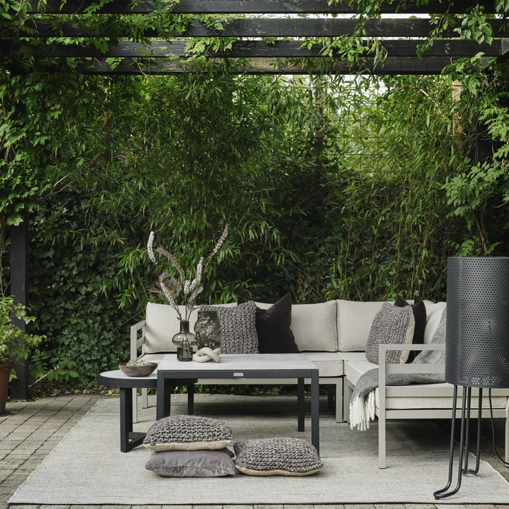 Brafab Weldon utesofa i beige under pergola med grønne planter, gulvputer og sort lykt