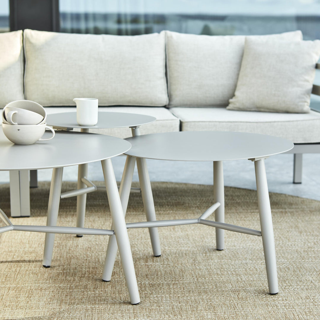 Brafab Weldon utesofa med lyse puter bak hvite settbord på teppe, kaffekopper