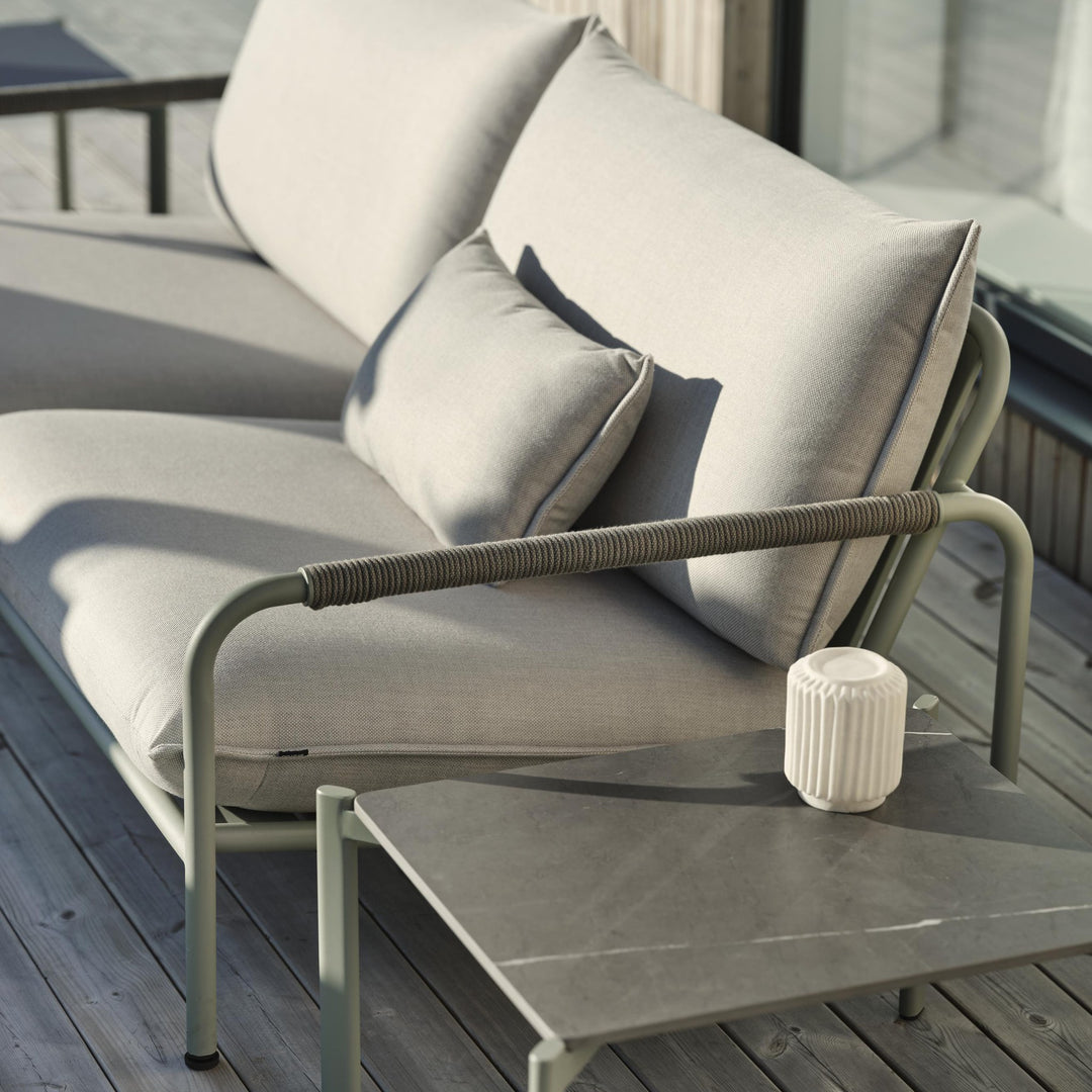 Brafab Lerberget loungesofa i dusty green med beige puter på terrasse, sidebord med hvit lyslykt
