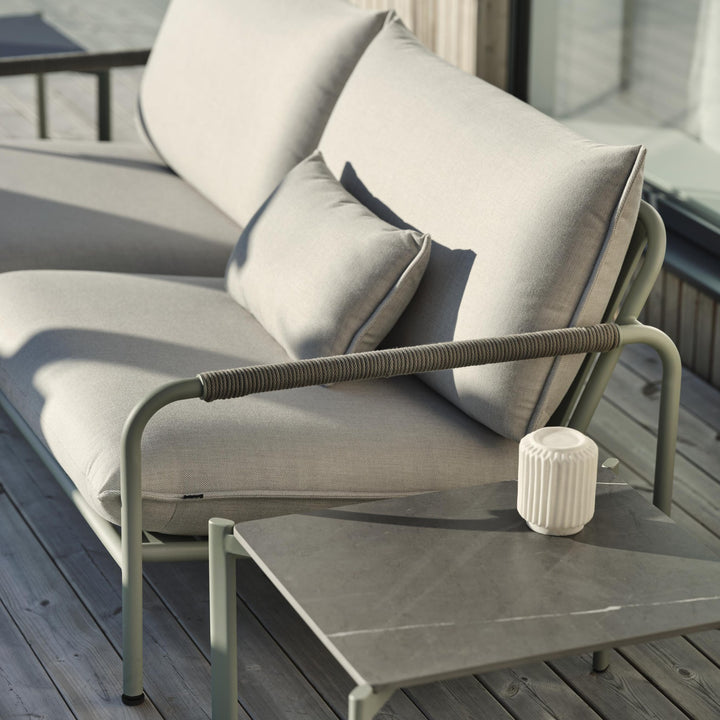 Brafab Lerberget loungesofa i dusty green med beige puter på terrasse, sidebord med hvit lyslykt