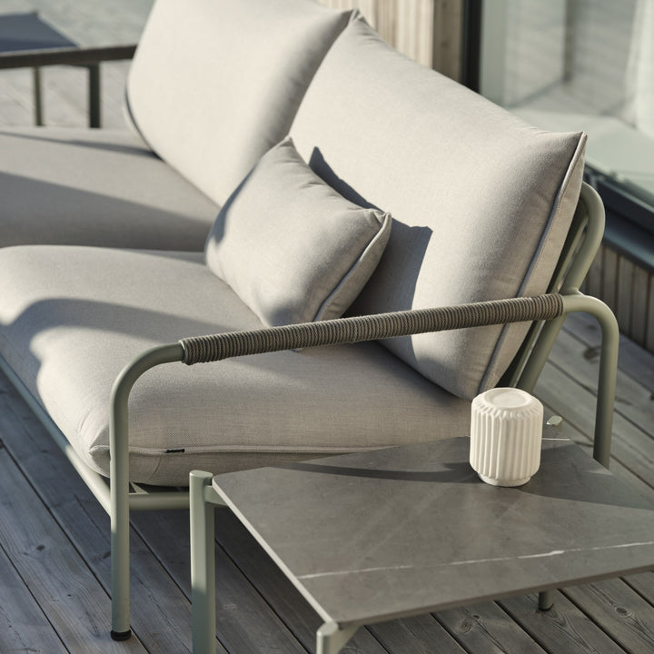 Brafab Lerberget loungesofa i dusty green med beige puter på terrasse, sidebord med lyslykt