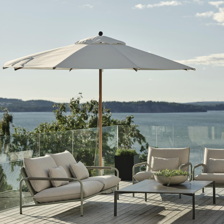 Brafab Lerberget utesofa med beige puter under parasoll på terrasse med havutsikt