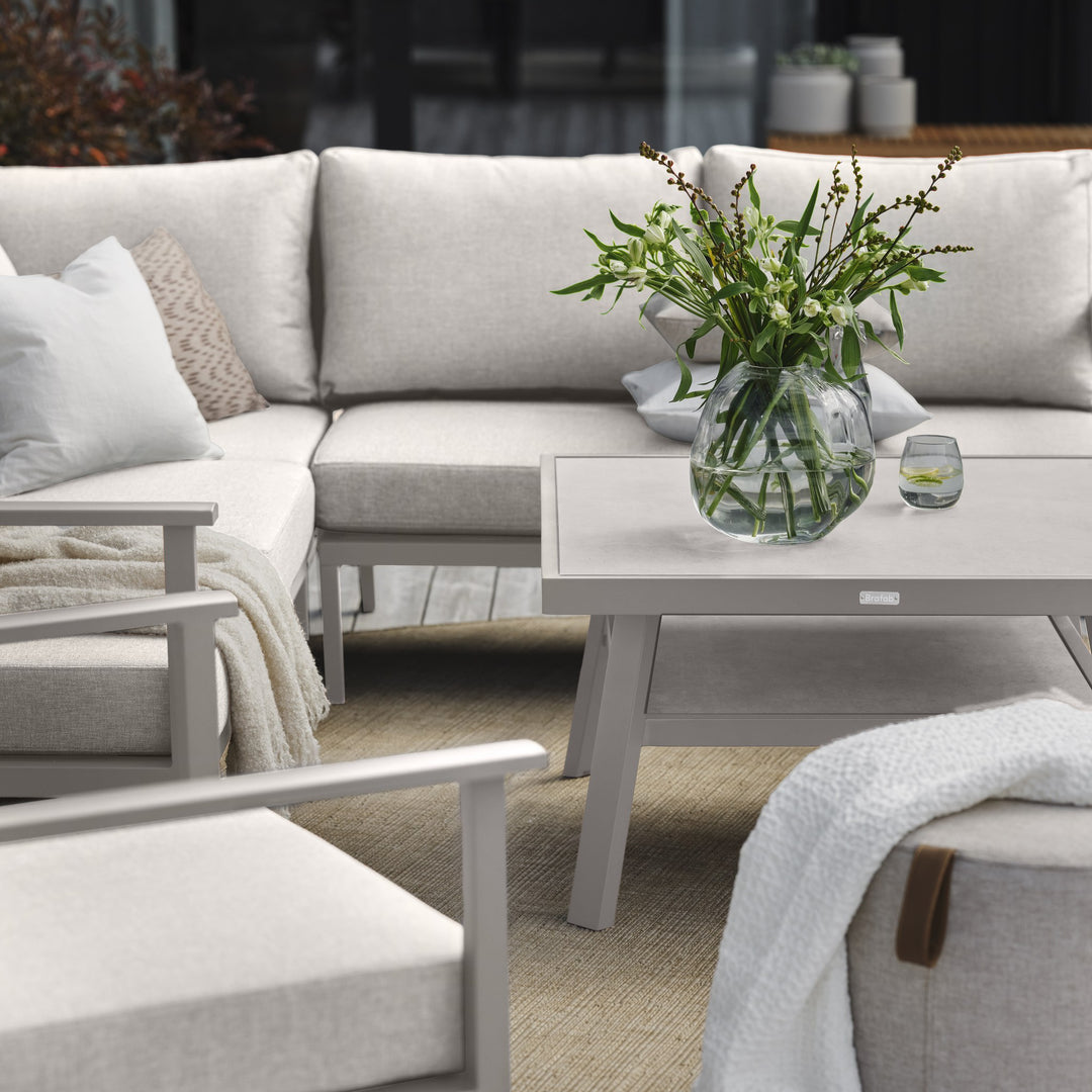 Brafab Samvaro Lounge modulsofa i beige med lysegrå ramme, bord med blomstervase og puff på terrasse