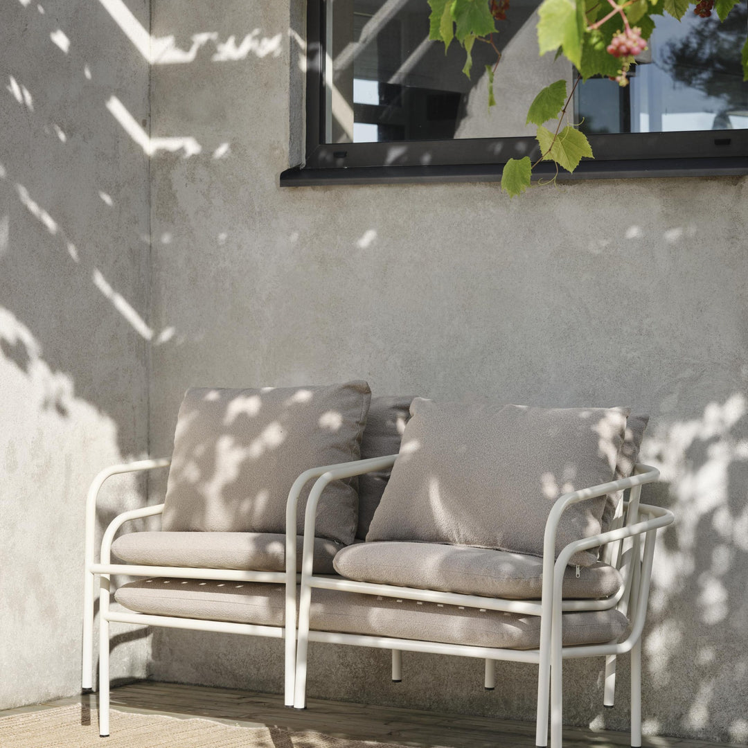 Brafab Bendt sofa med hvit ramme og beige puter på terrasse med solflekker, grå vegg og vinranke