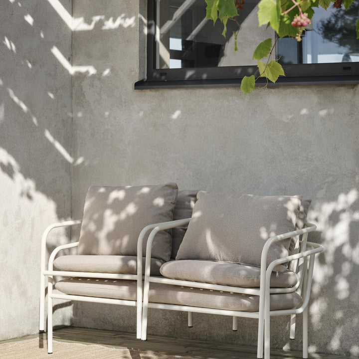 Brafab Bendt sofa med hvit ramme og beige puter på terrasse med solflekker, grå vegg og vinranke