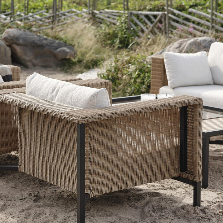 Brafab Shell utesofa i naturfarget kunstrotting med hvite puter ved klitter og sanddyne