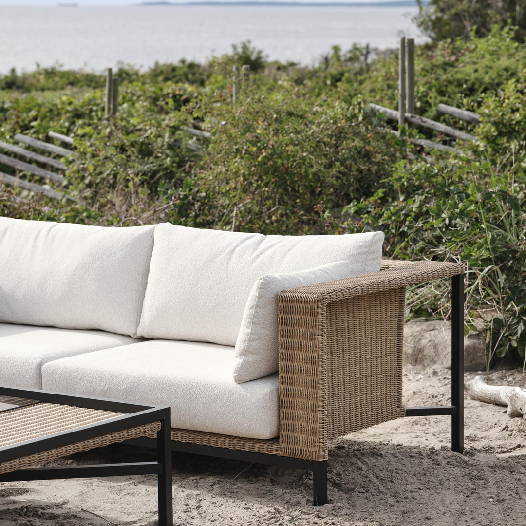 Brafab Shell utesofa i naturfarget kunstrotting med hvite puter ved havet og klitter med busker