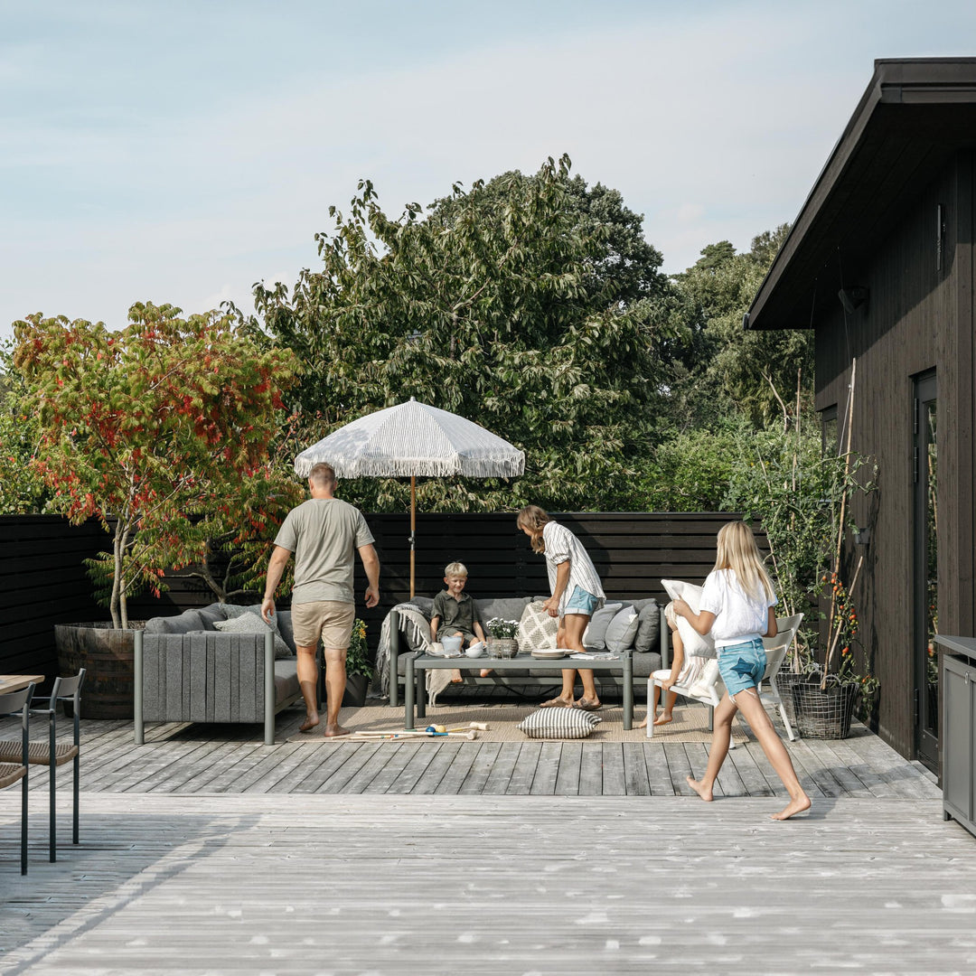 Brafab Brad loungesofa i grått med mønstret parasoll på terrasse, familie samlet ved sort hus