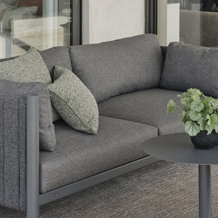Brafab Brad loungesofa i antrasitt med mønstret pute, grønn plante og sort sidebord