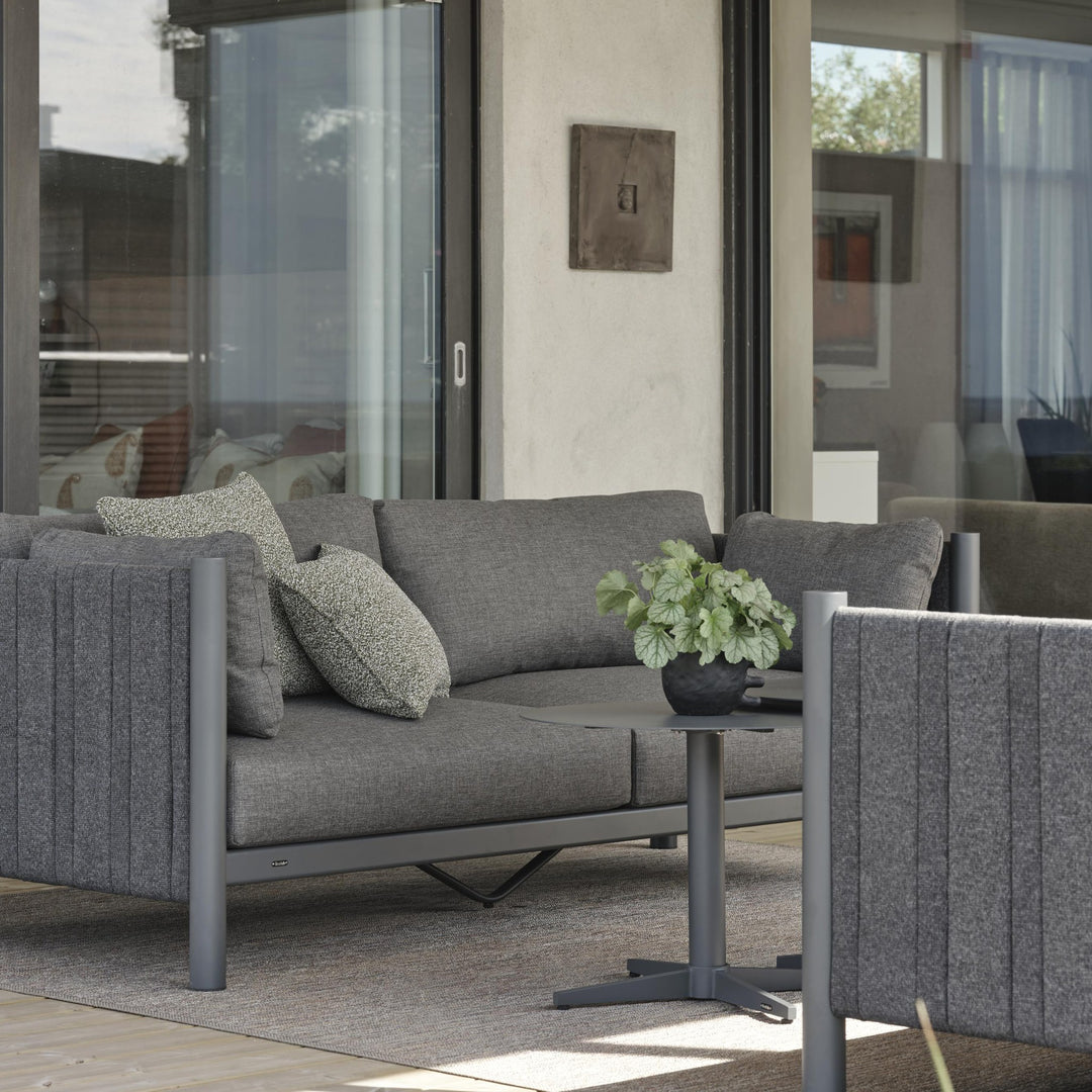 Brafab Brad loungesofa i antrasitt med mønstrede puter, plante og sidebord ved skyvedør