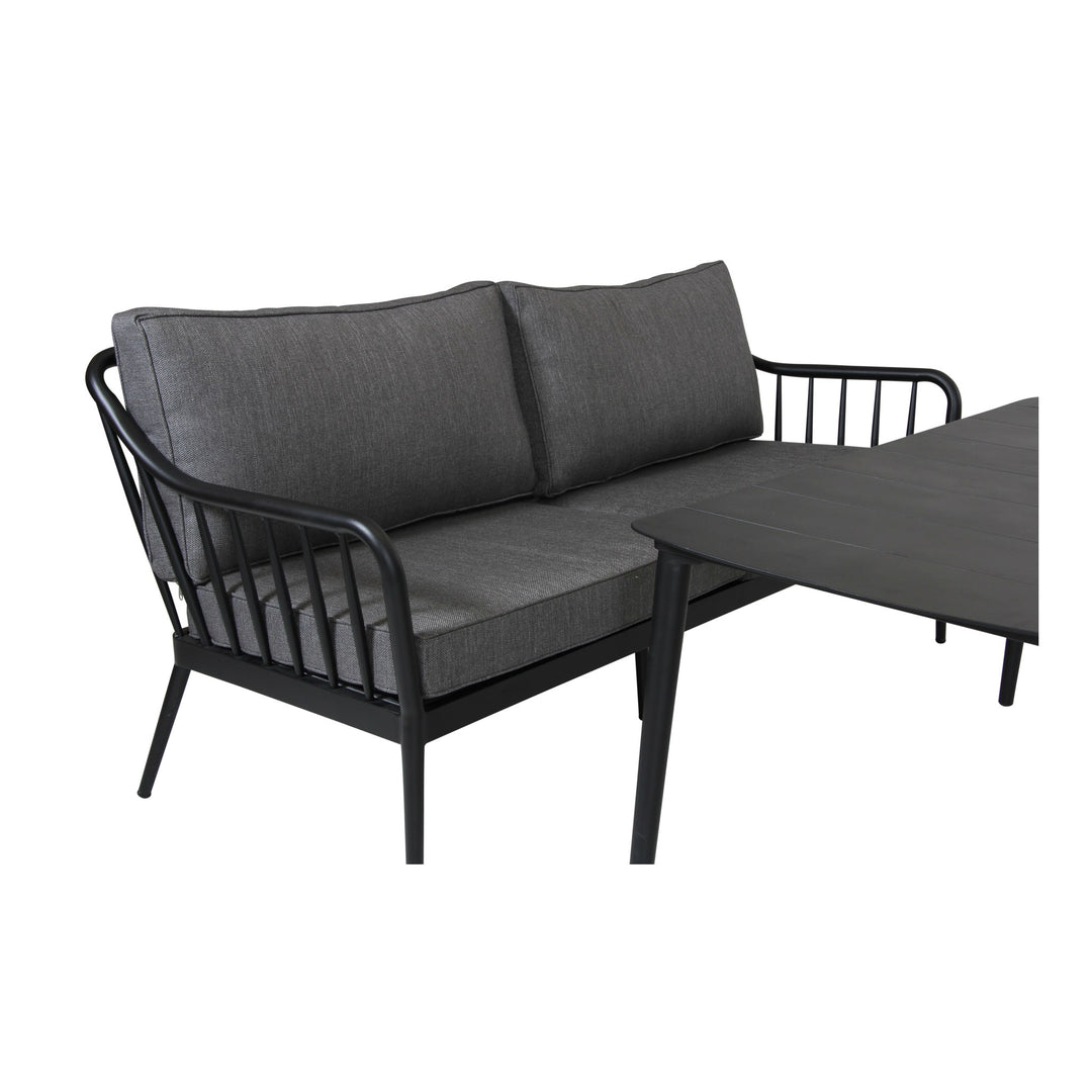 Brafab Coleville utesofa i sort aluminium med mørkegrå puter, ved siden av sort spisebord