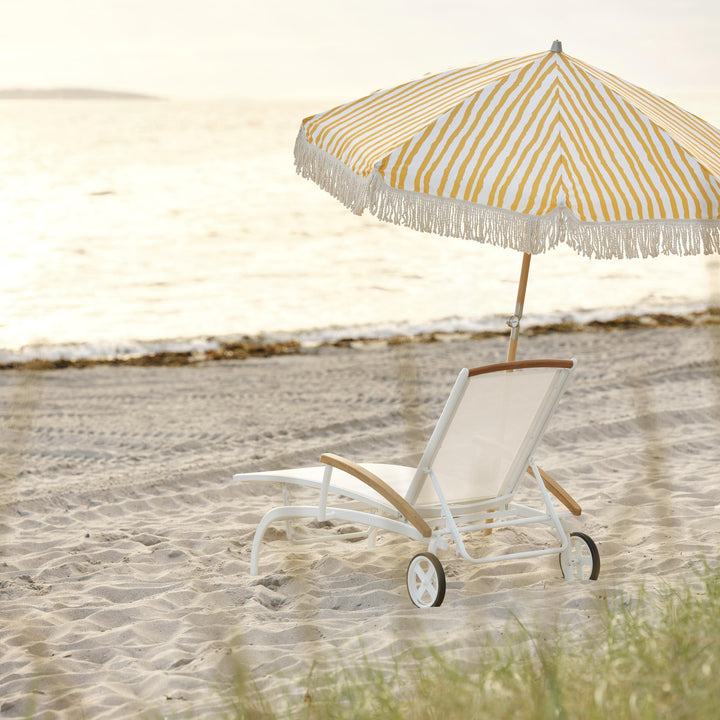 Brafab Gatsby parasoll i gule og hvite striper med frynser på stranden, solseng i sanden