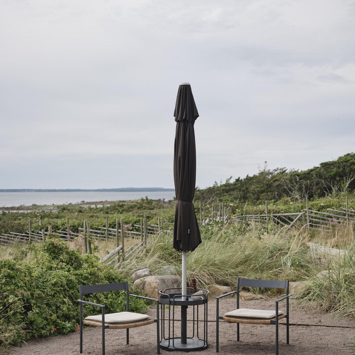 Brafab Shady parasollfot i antrasitt med sammenslått parasoll, to stoler ved strand med havutsikt