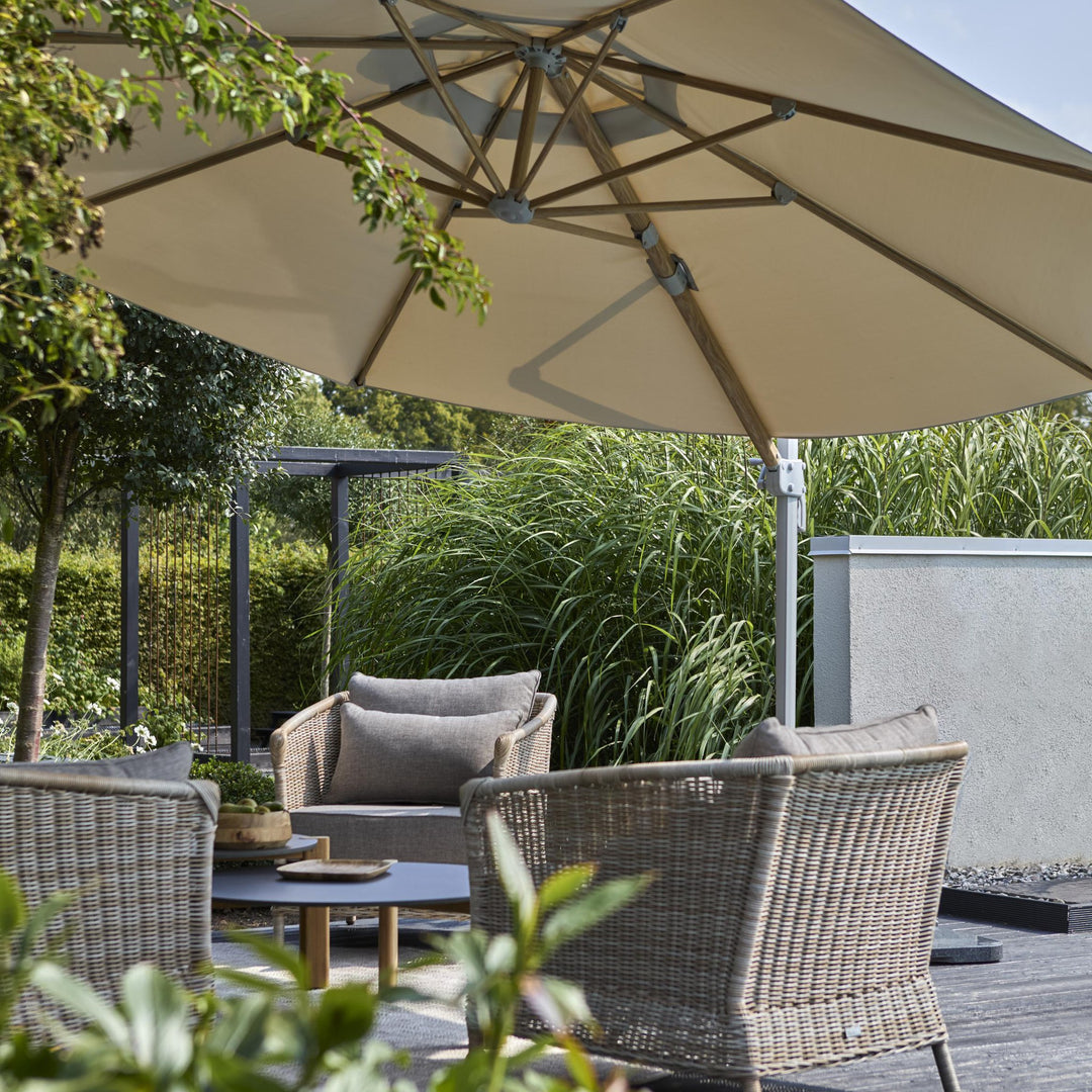 Brafab Luzzi parasoll i beige over terrasse med kurvstoler, planter og prydgress