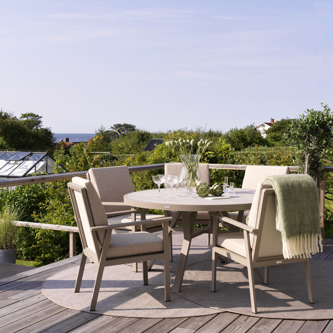 Brafab Samvaro spisestol i beige med puter ved rundt spisebord på terrasse med havutsikt