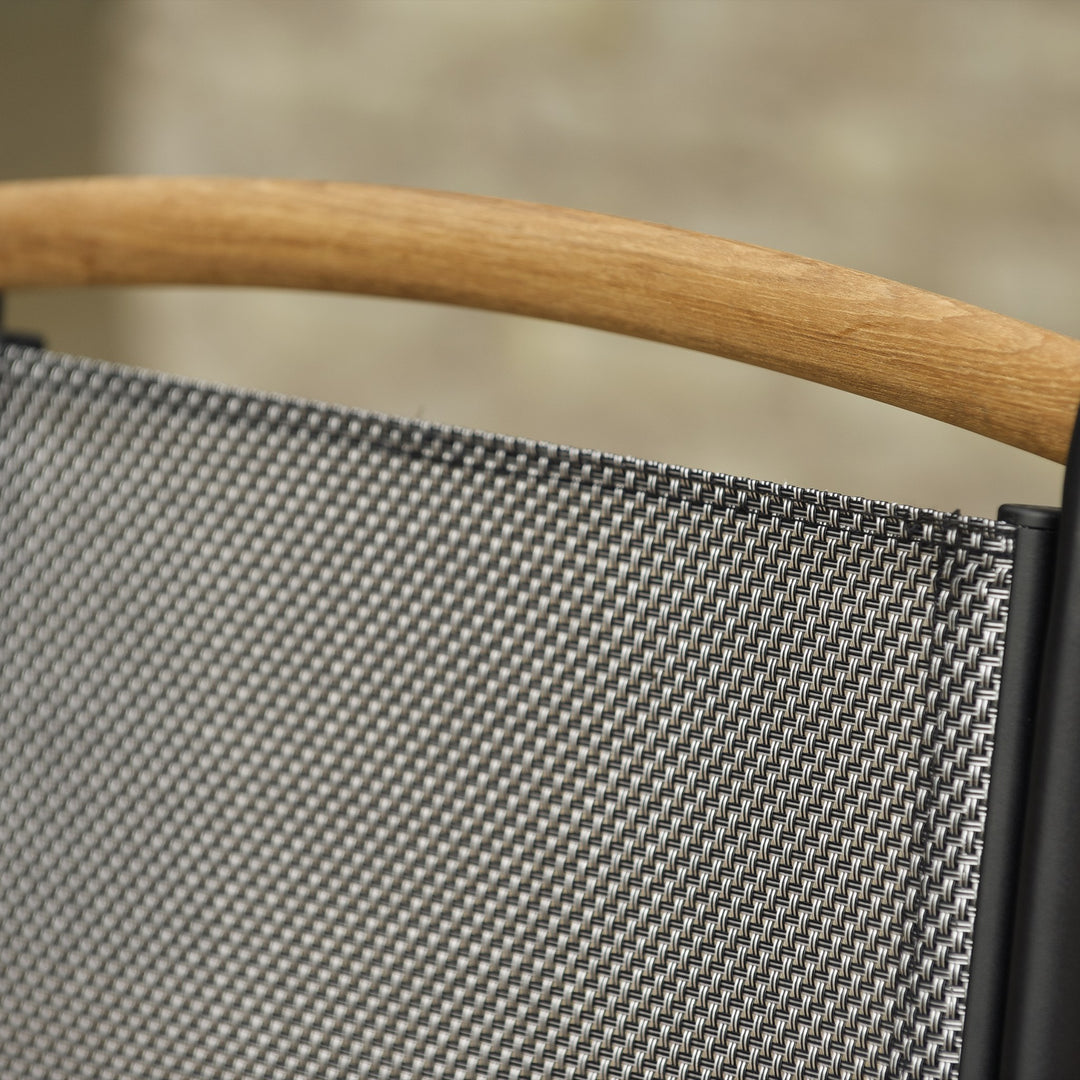 Brafab Andy spisestol i sort tekstil med teak armlener ved mørkt hagebord ved basseng