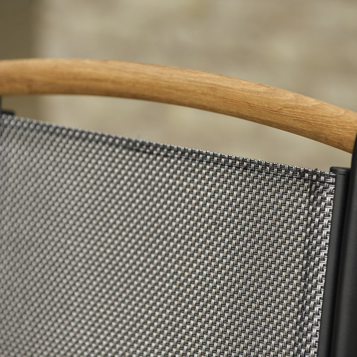 Brafab Andy spisestol i sort tekstil med teak armlener ved mørkt hagebord ved basseng