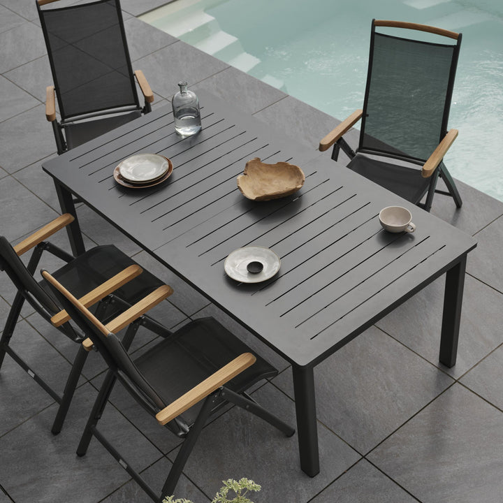 Brafab Andy spisestol i sort med teak armlener ved mørkt bord ved basseng, sett ovenfra