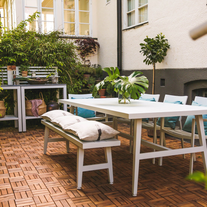 Brafab Vevi benk i hvit på terrasse med hvitt spisebord, grønne planter og turkise puter