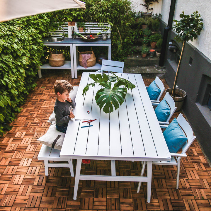 Brafab Vevi benk i hvit ved hvitt spisebord på terrasse, med grønne planter og turkise puter