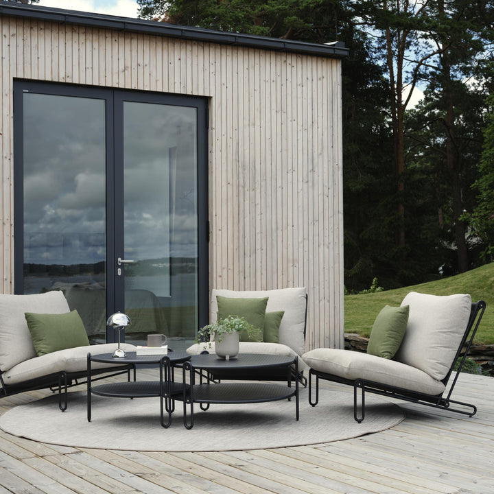 Brafab Blixt hagestoler i sort med beige puter på terrasse, grønne puter og svarte bord ved sjøen