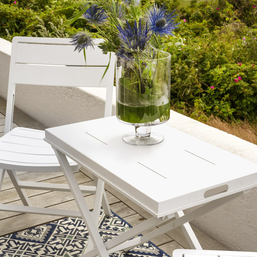 Brafab Wilkie klappstol i hvit ved klappbord med grønn vase og blå blomster på terrasse