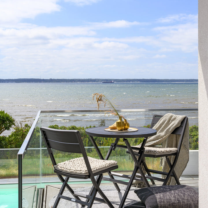 Brafab Wilkie klappstol i sort med rundt bord på terrasse med havutsikt og strikkede seteputer