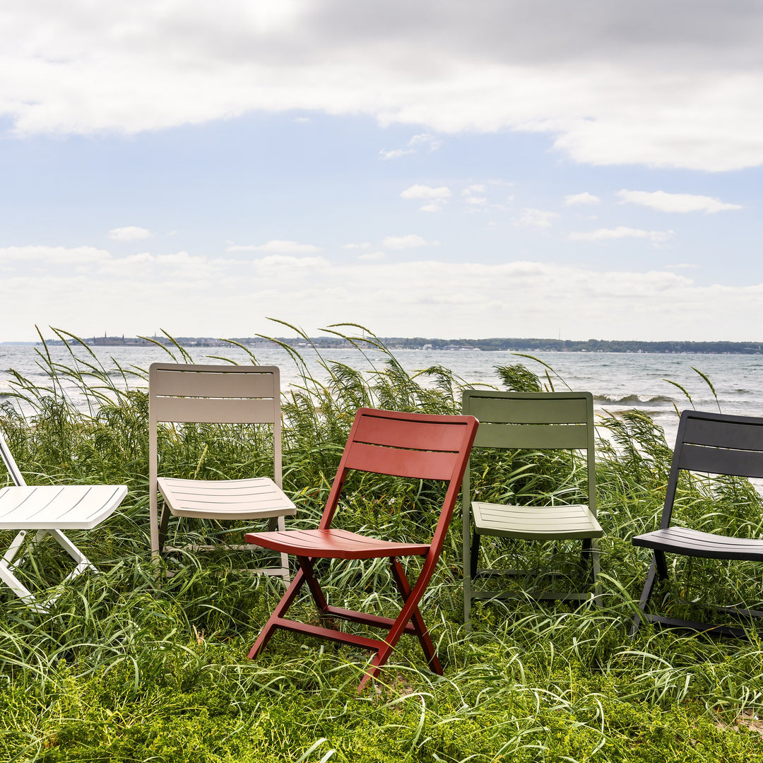 Brafab Wilkie klappstol i flere farger på rad i strandgress ved sjøen med hav i bakgrunnen