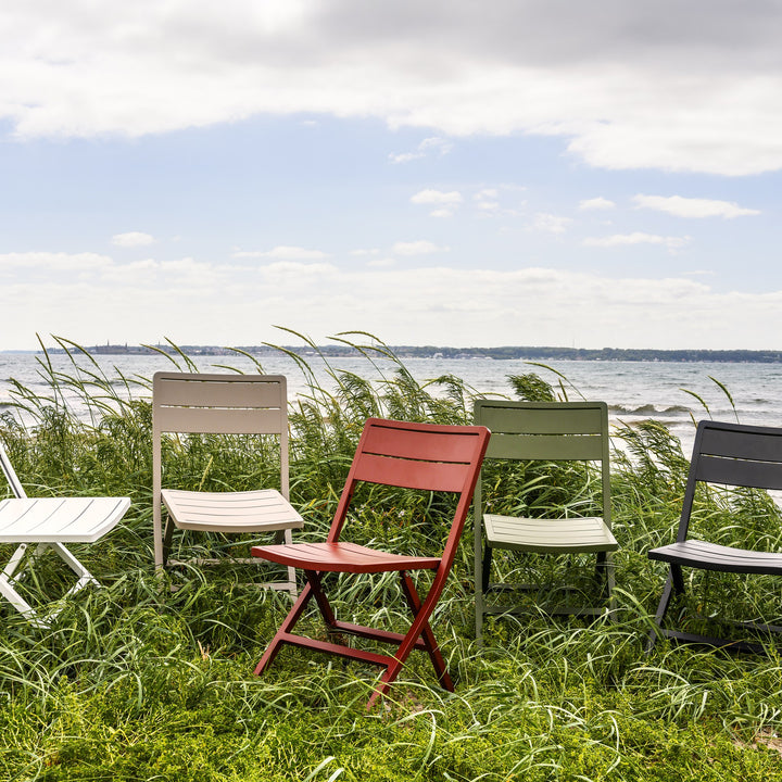 Brafab Wilkie klappstol i flere farger på rad i strandgress ved sjøen med hav i bakgrunnen