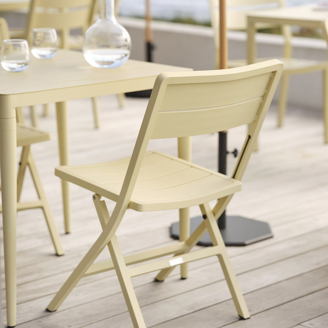 Brafab Wilkie klappstol i lys gul, nærbilde sett bakfra ved bord på terrasse ved sjøen