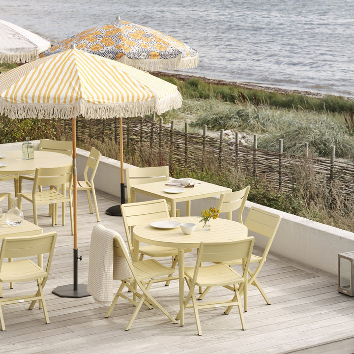 Brafab Wilkie klappstoler i lys gul på terrasse ved sjøen, med gulstripete parasoller