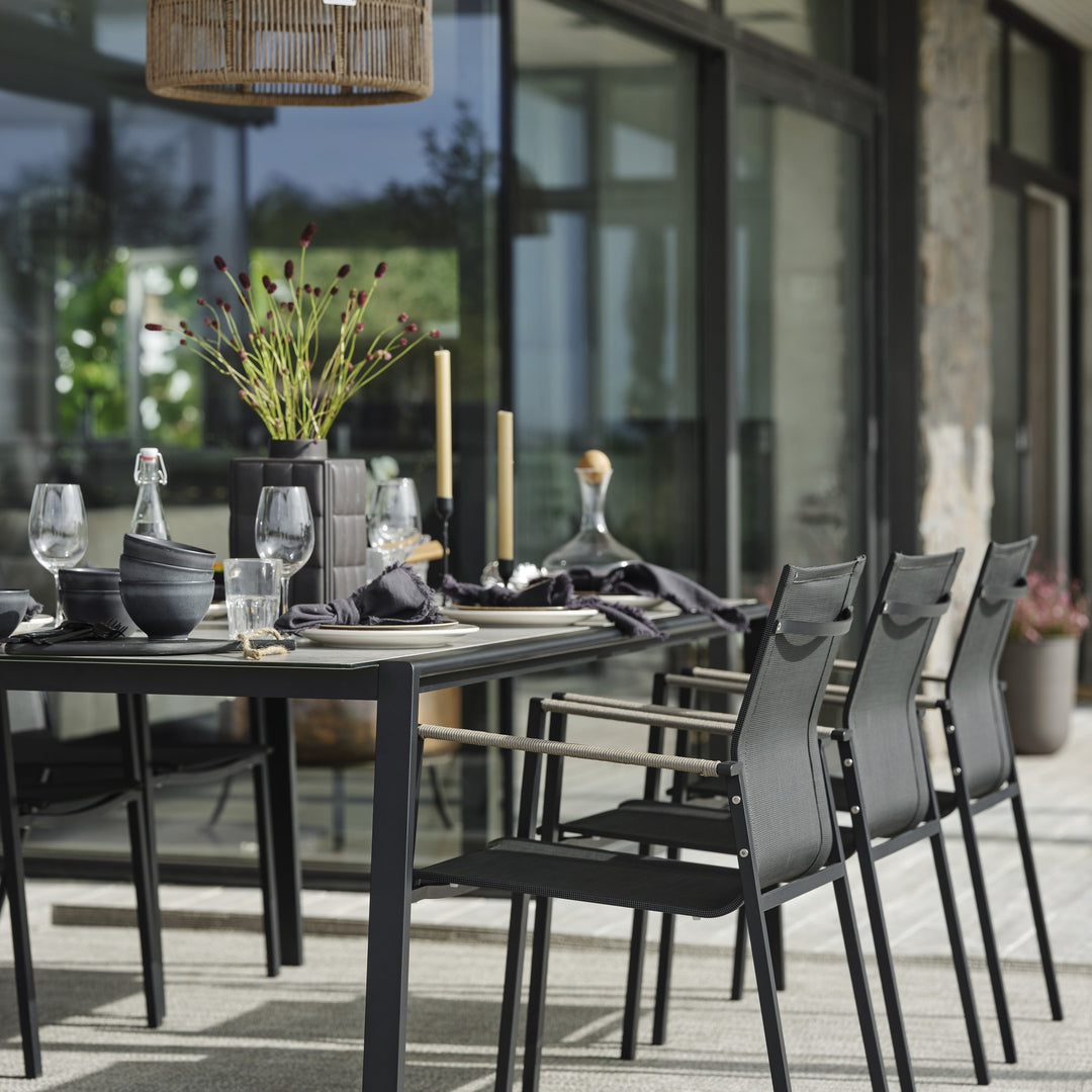Brafab Lyra spisestol i sort på terrasse ved sortdekket bord med glass, tallerkener og tørkede blomster