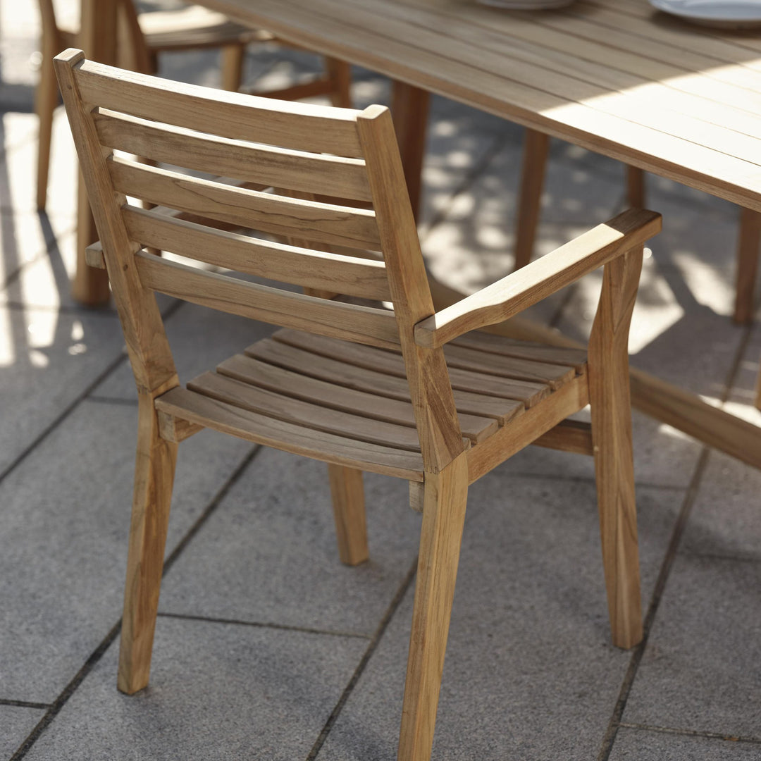 Brafab Keros spisestol i teak, sett bakfra ved teakbord på steinheller i sollys