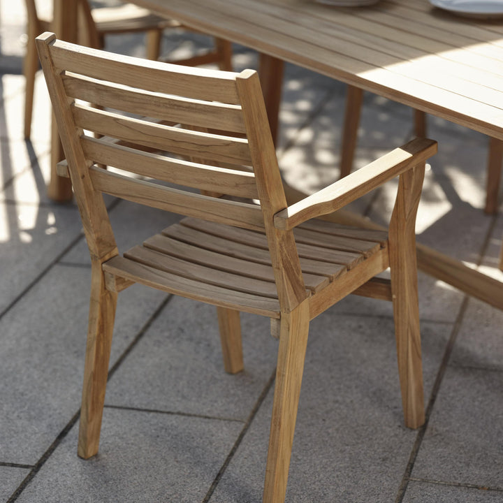 Brafab Keros spisestol i teak, sett bakfra ved teakbord på steinheller i sollys