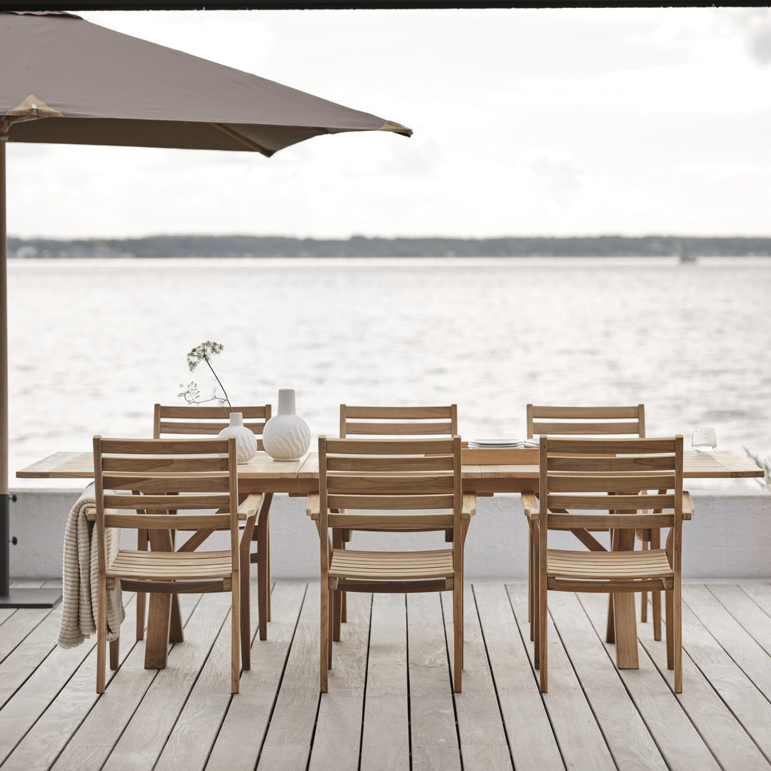Brafab Keros spisestol i teak ved langbord på terrasse ved sjøen under parasoll
